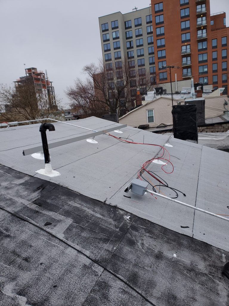 Flat roof under solar panel installation with mounting rails and electrical wiring in urban residential area