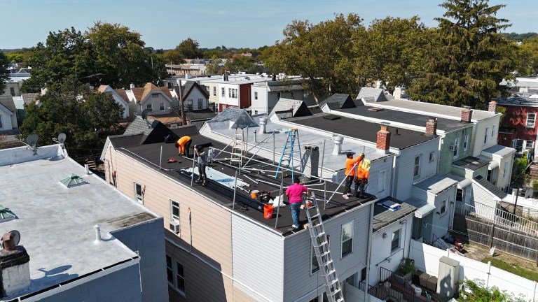 Aerial view of solar panel installation crew working on flat residential rooftop in urban neighborhood