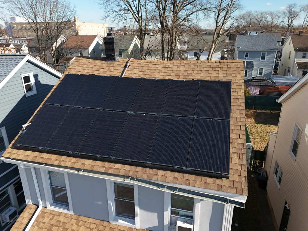 Aerial view of a full solar array on the pitched roof of a New York house, on a tree-lined residential street