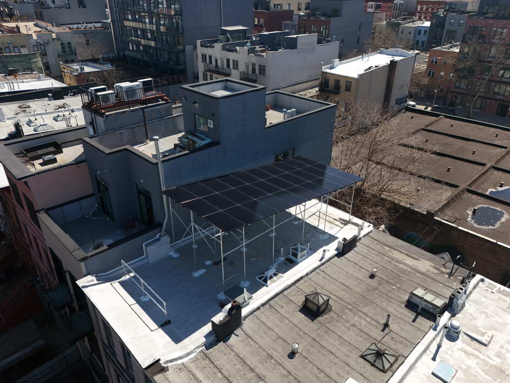 Aerial view of a solar canopy built over a flat city rooftop, keeping the roof deck usable underneath