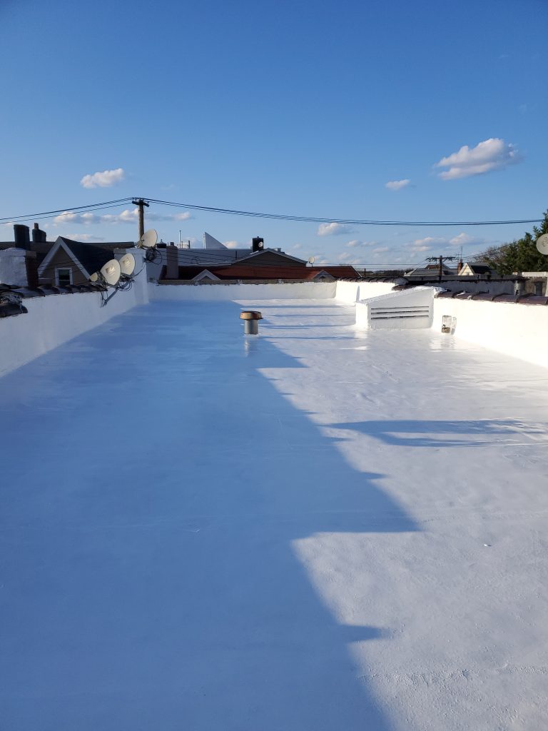 White coated flat roof waterproofing system on residential building under clear blue sky