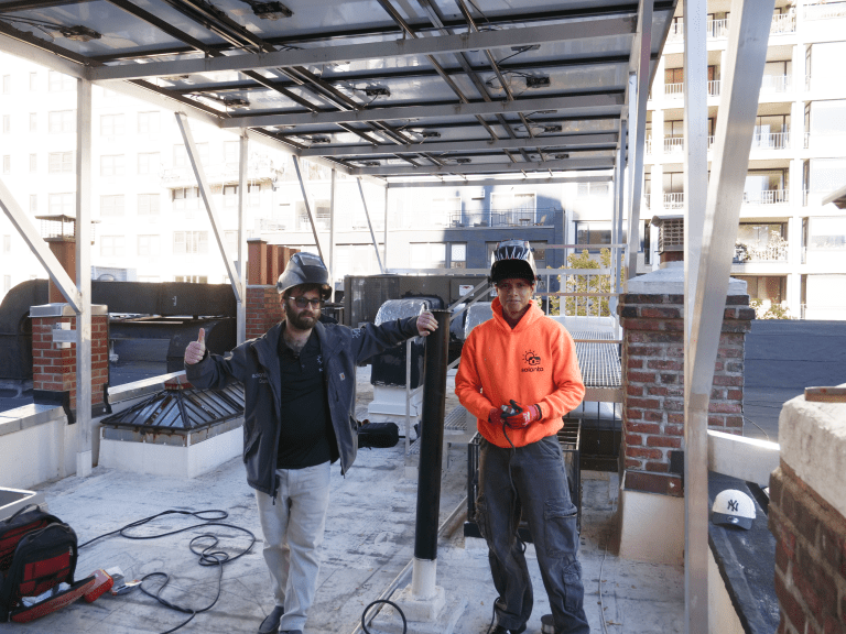 Solar installation technicians proudly standing on residential rooftop under solar canopy structure in urban building setting