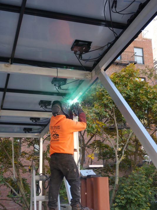 Worker welding metal frame for rooftop solar panel installation on residential building