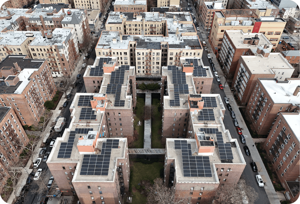 Drone view of multiple apartment buildings with rooftop solar panel arrays installed across a residential complex.