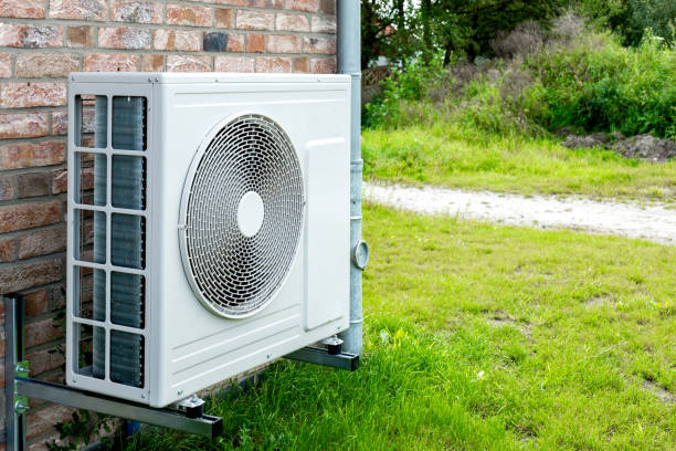 Residential HVAC outdoor condenser unit mounted on brick wall next to grassy yard