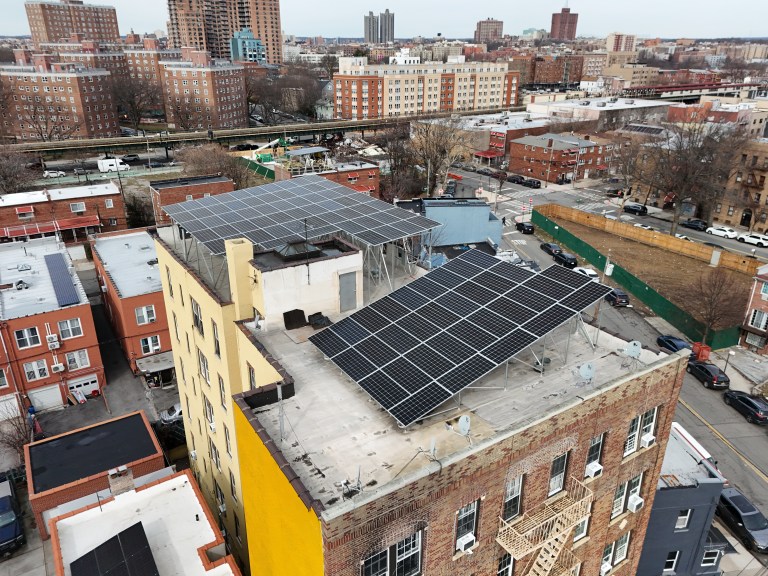 Aerial view of a commercial industrial building with rooftop solar panels surrounded by vehicles, trucks, and school buses.