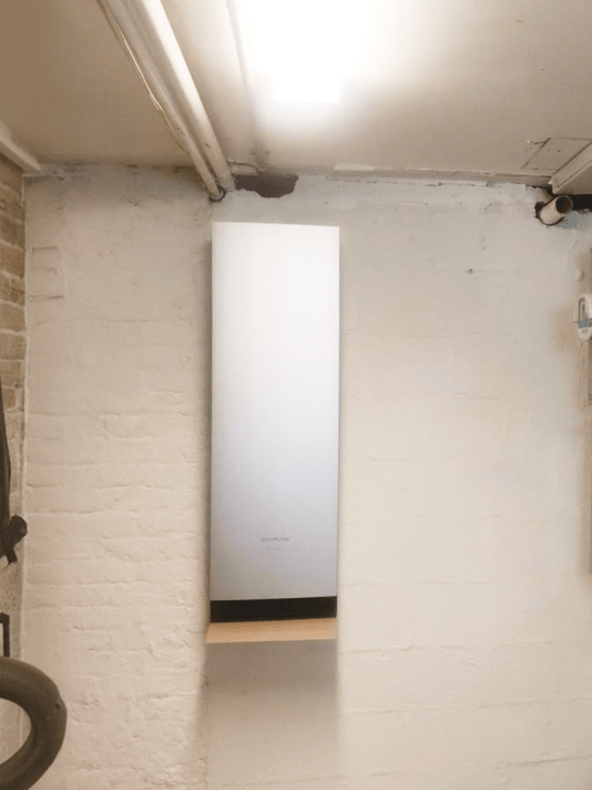 Wall-mounted home battery backup system installed in a basement beside residential electrical panels and utility meters.